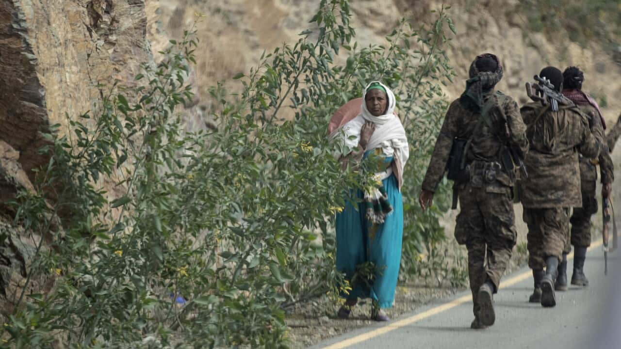 A woman walks past Ethiopian government soldiers by the side of a road north of Mekele, in the Tigray region of northern Ethiopia