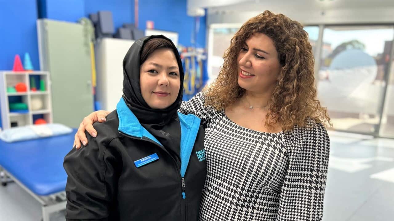 A woman in a blue and black jacket stands next to another woman in a black and white checked top.