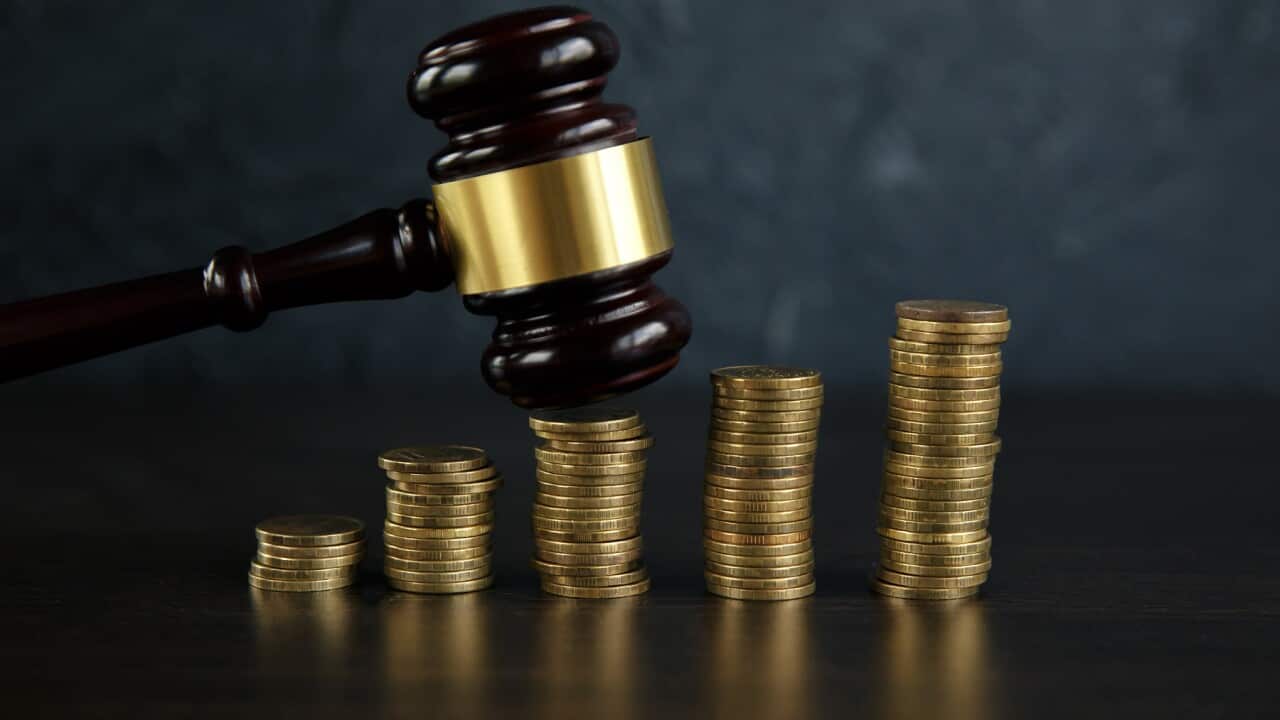 Close-up Of A Judge's Hand Holding Gavel Over Stacked Golden