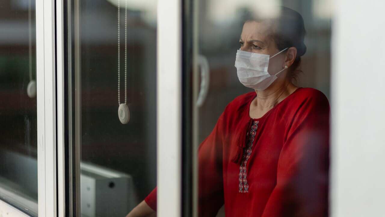 Woman looks outside the window wearing a mask