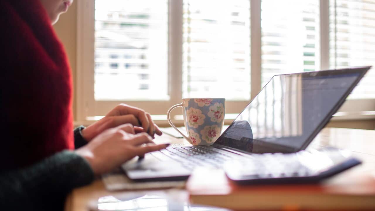A woman's hands type on a laptop, placed next to a coffee mug on a table at home