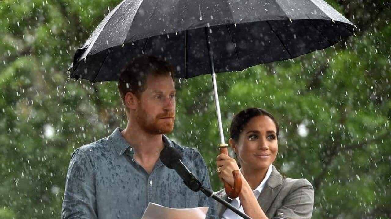 Meghan holds an umbrella over Harry as he delivers a speech in Dubbo.