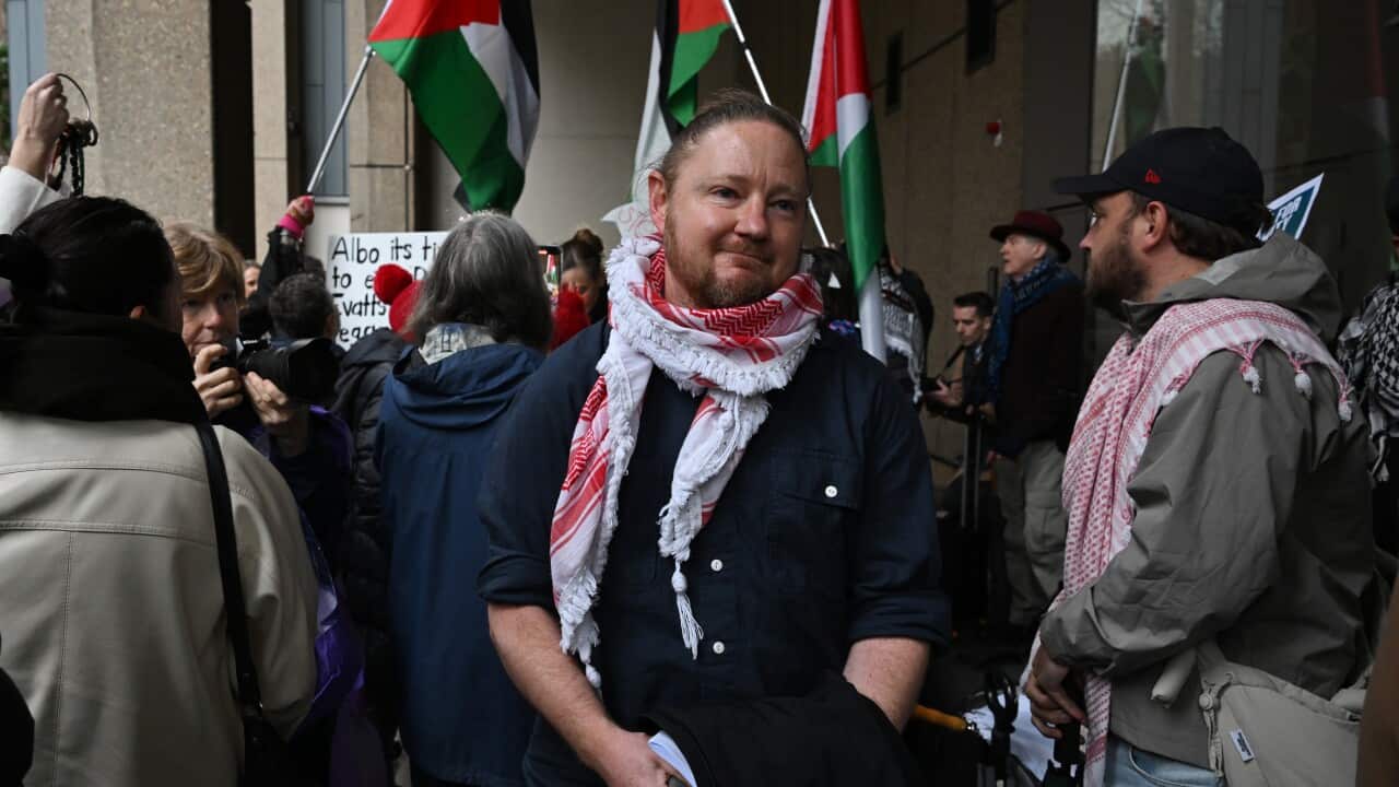A man stands outside a court, surrounded by crowds of people.