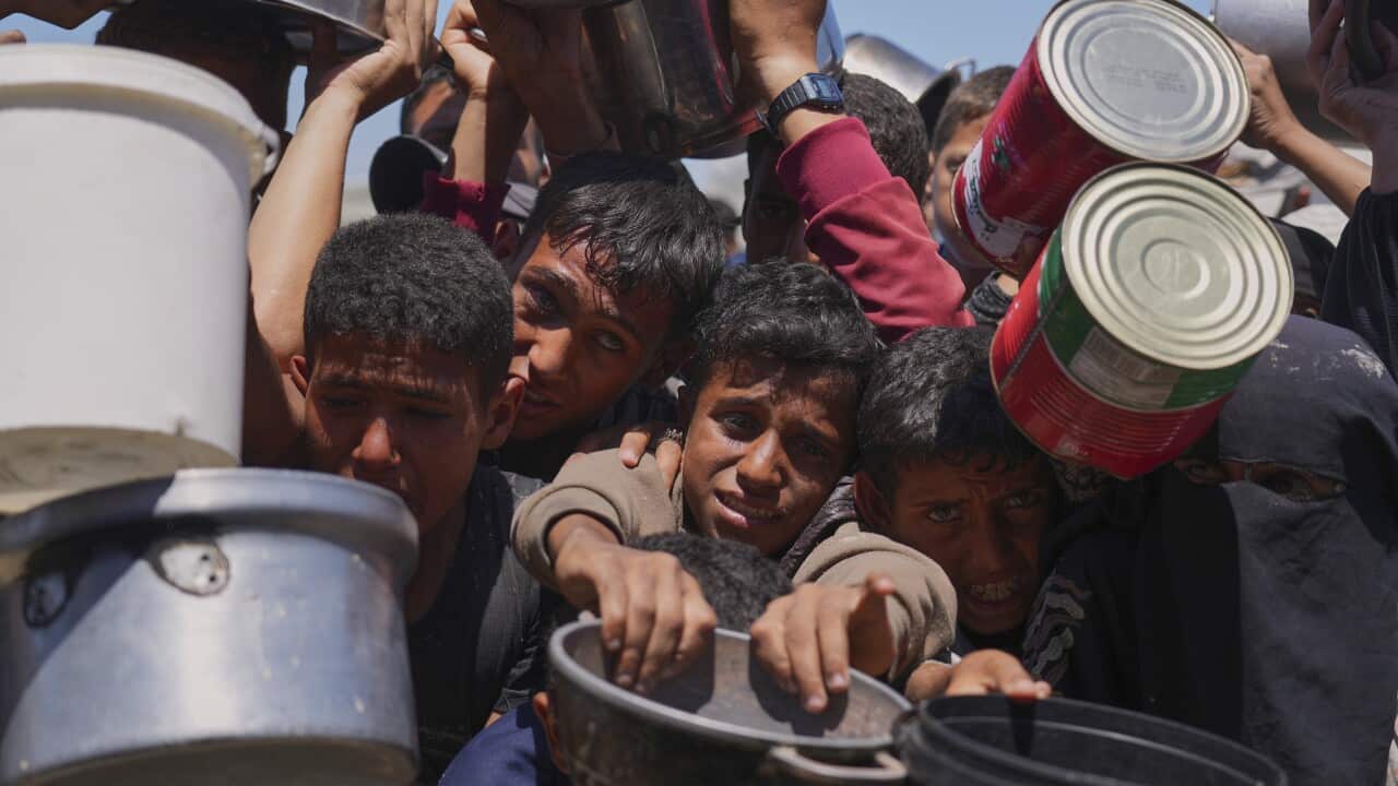 A group of people holding empty pots and cans is pushing forward. A young child looks distressed in the centre.