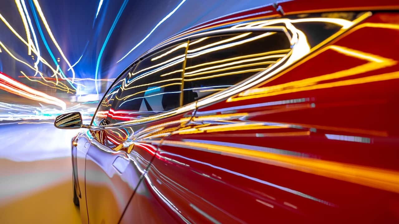Red electric powered car drives on city highway while night - streaking street lights