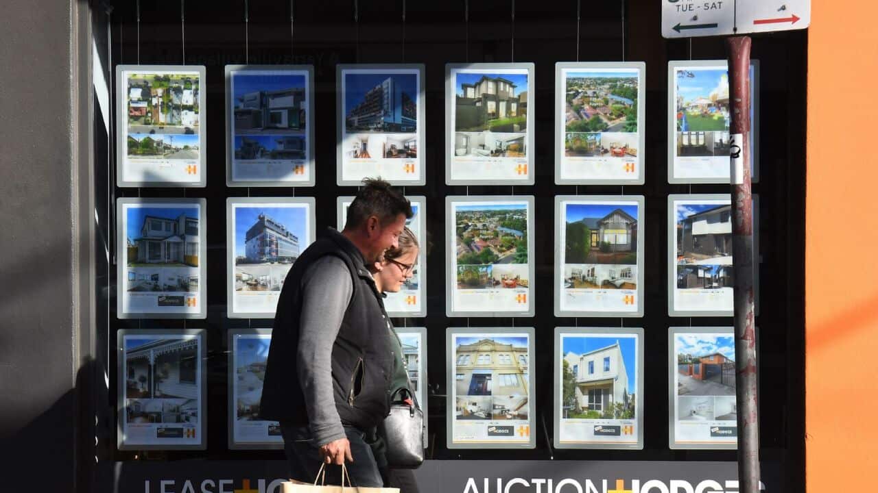 A couple walks past a real estate agent's window advertising houses for sale and auction in Melbourne