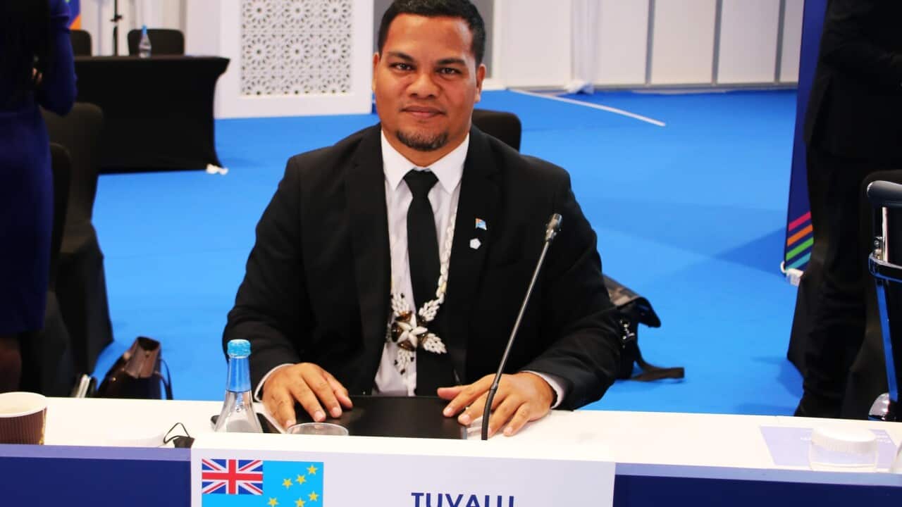 Tuvalu Foreign Minister Simon Kofe seated at a table. On the table is a sign with the Tuvalu flag on it.