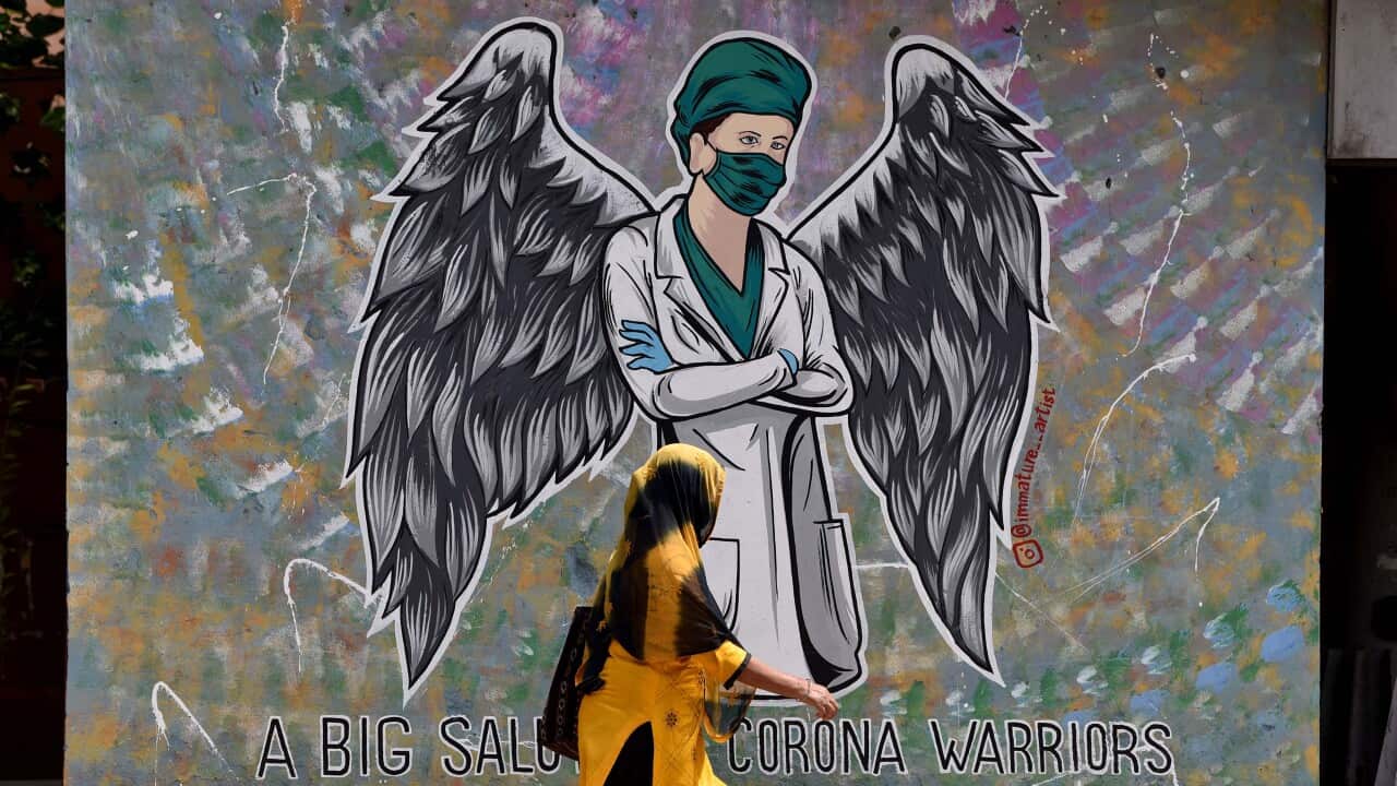 A woman walks past a wall graffiti in respect of Corona warriors