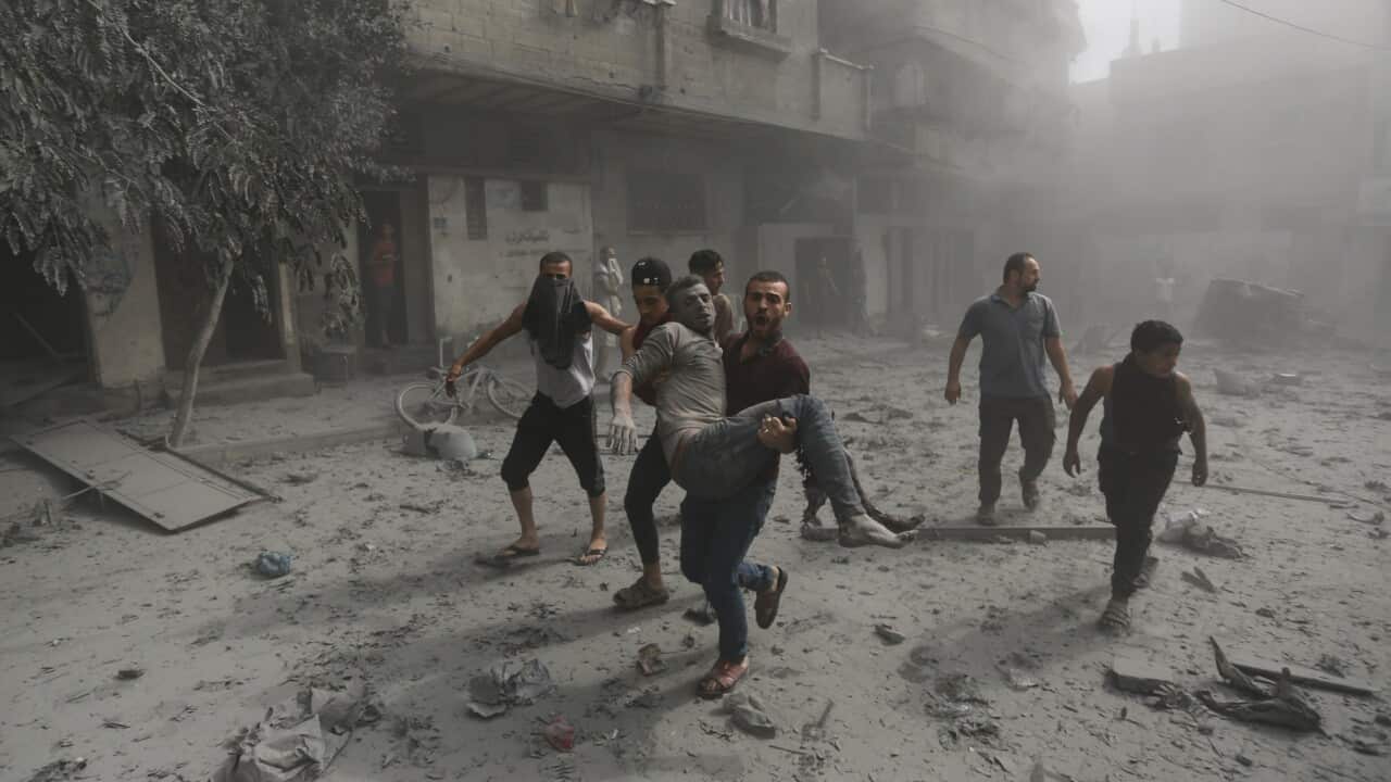 People running along a street. One is carrying a man who is injured.