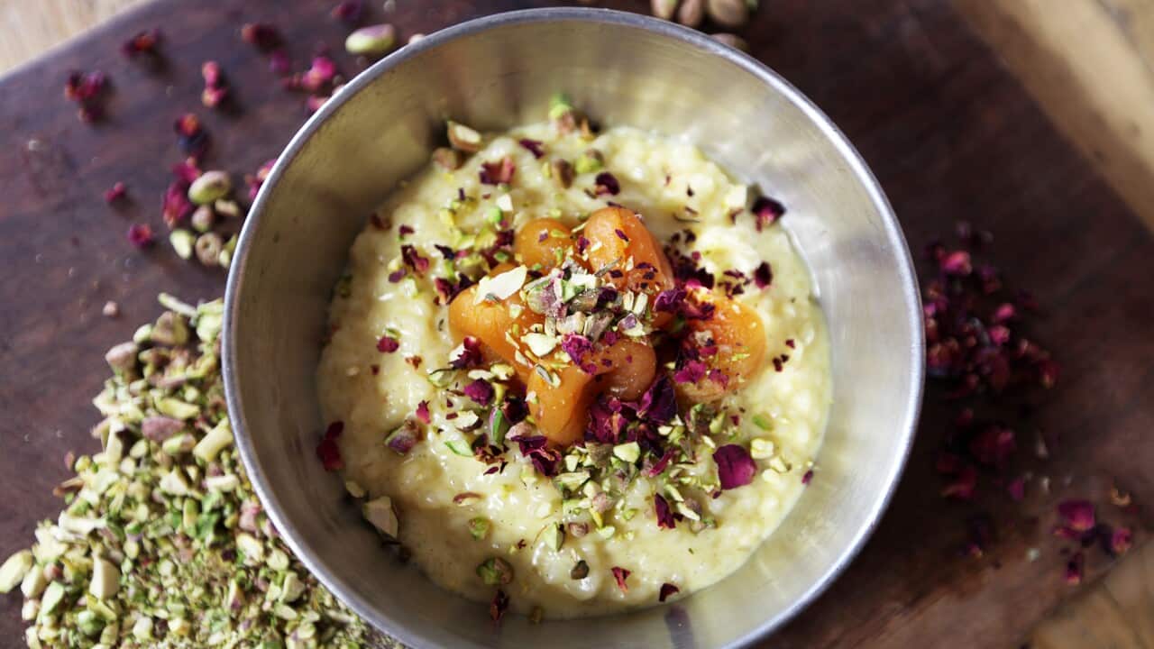 A silver bowl holds a creamy pidding, topped with fruit, pistachios and dried rose petals.