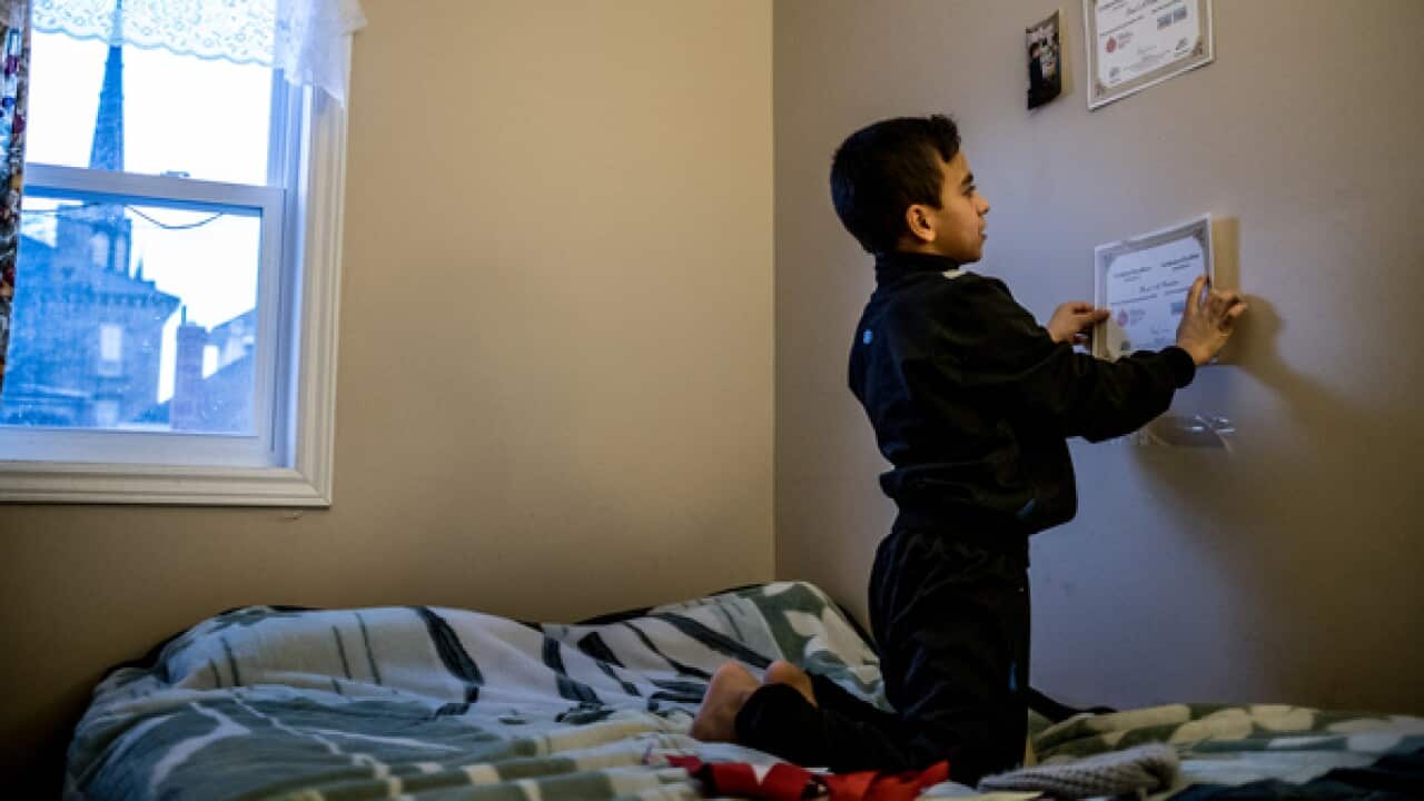 Basel Alrashdan, 11, tapes achievement certificates from school and community events to his bedroom wall in Charlottetown, Canada on Dec 9, 2016.