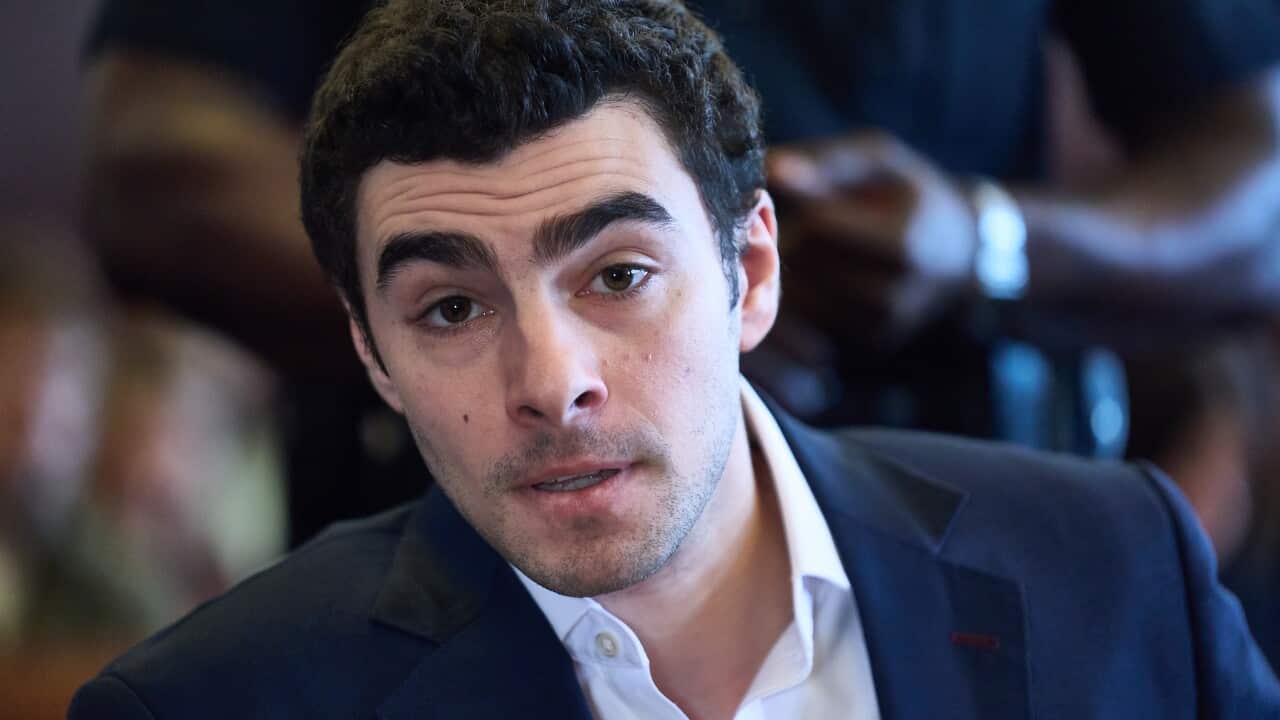 A young white man with short, dark hair wearing a navy blazer and white shirt