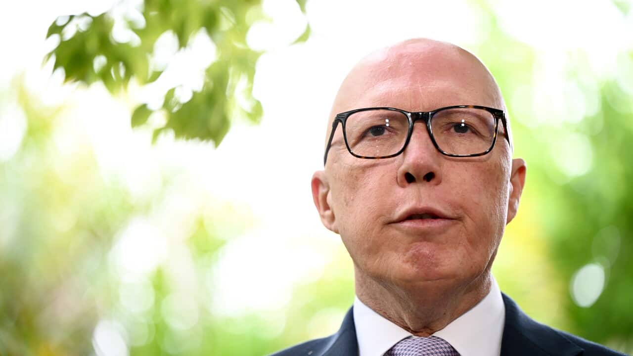 A man (Peter Dutton) wearing black-rimmed glasses, a formal suit, and a tie looks forward with a neutral expression on his face.