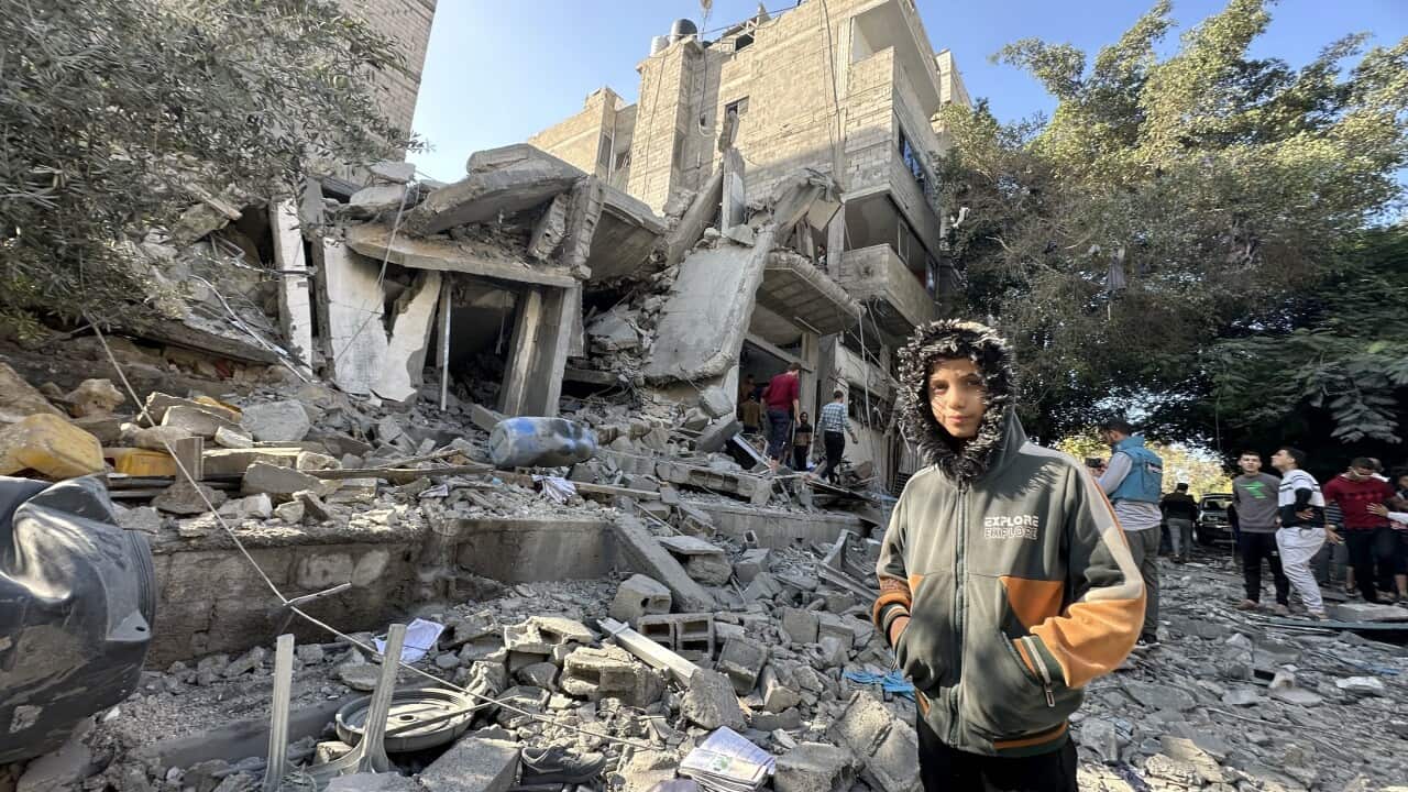 A boy stands in front of a destroyed building.