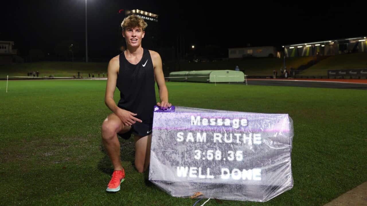 A young boy kneels beside a sign in a field displaying the words 'Message Sam Ruthe 3.58.35 well done'.