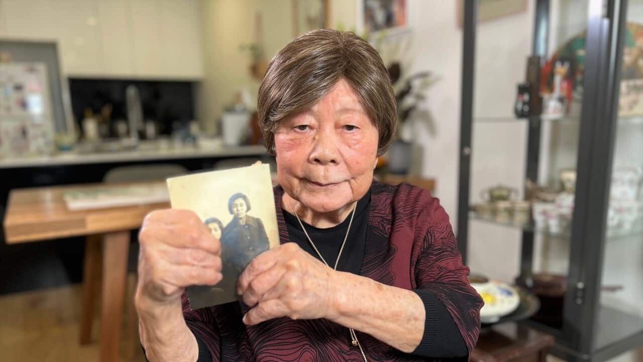A woman wearing a burgundy top sits in a chair and holds an old photo. 