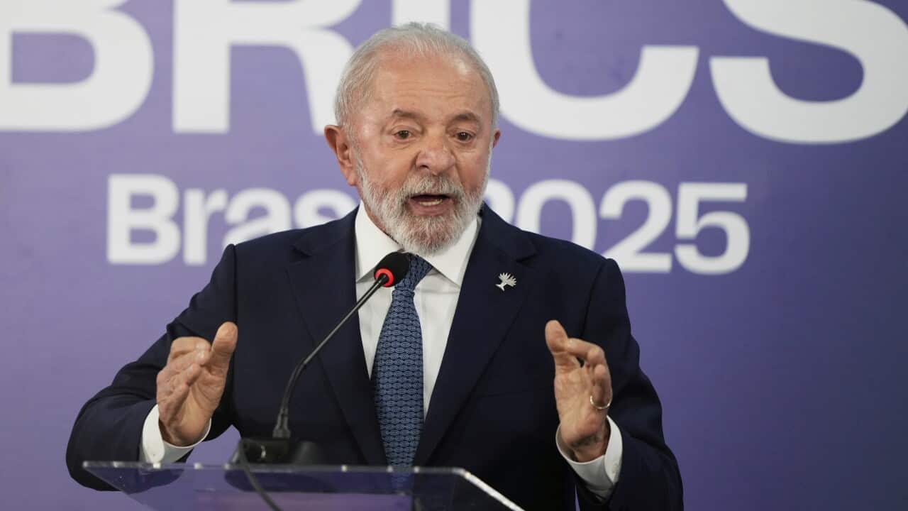 A man wearing a suit at a podium. There is a sign behind him that reads BRICS Brasil 2025