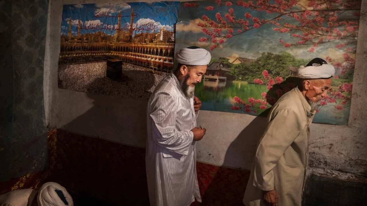 Uighur men pass a poster showing Mecca in the Xinjiang region