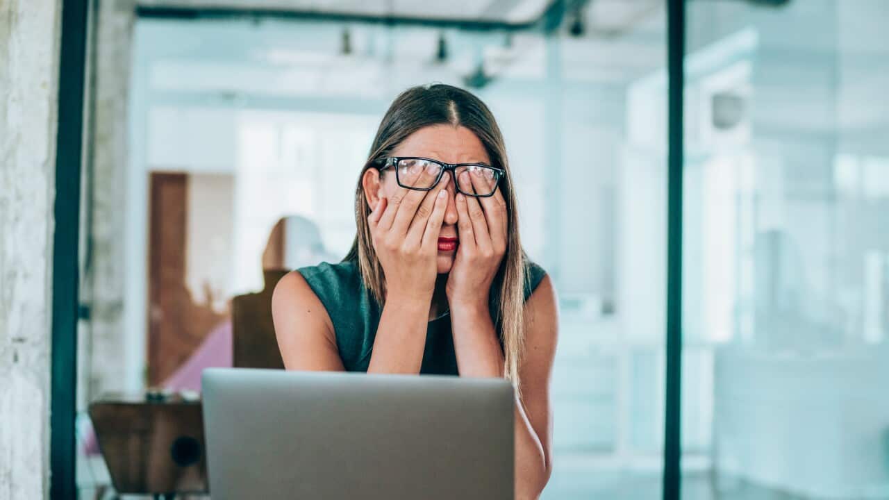 A woman sitting at a desk at her laptop with her hands on her face.