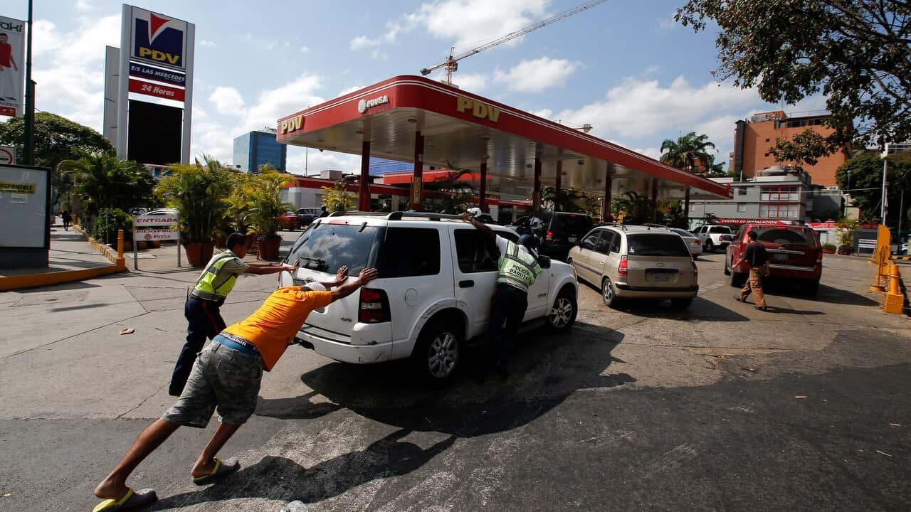People push a car without gas to one of the few fuel stations that has its own electric generator during an electricity blackout in Caracas.