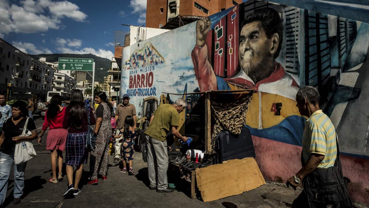 People pass a defaced mural of Venezuelan President Nicolas Maduro in the center of Caracas, Venezuela