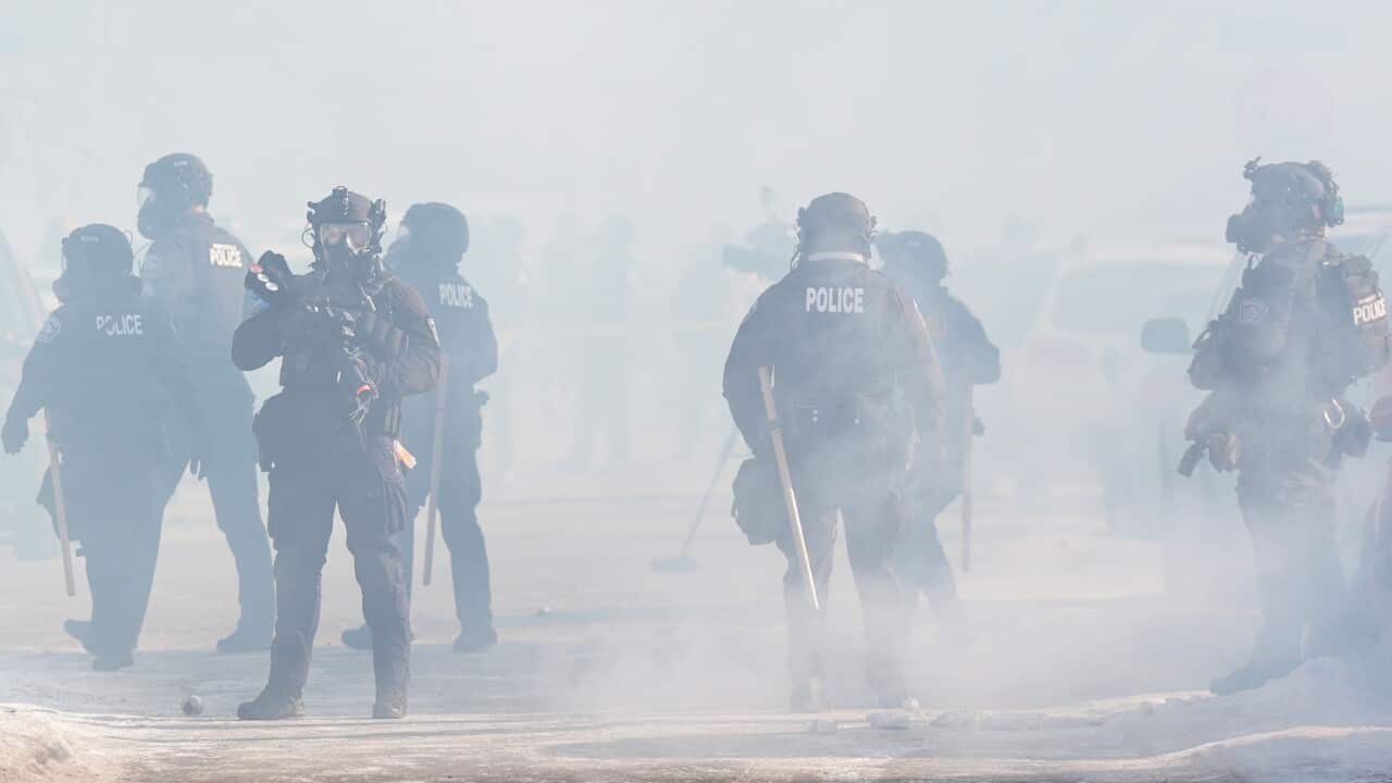 Armed police officers deploy tear gas in the street.