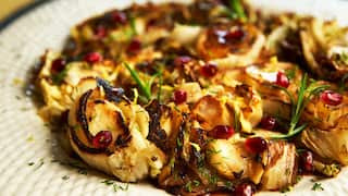 A cabage salad sits on a white plate withe a textured edge. Small sprigs of rosemary decorate the salad.