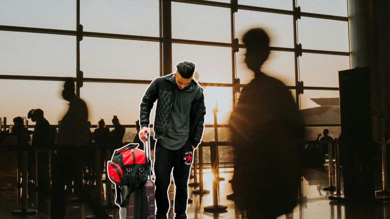 An Indian youth holding bag with his head down in disappointment superimposed on a busy airport crowd background.