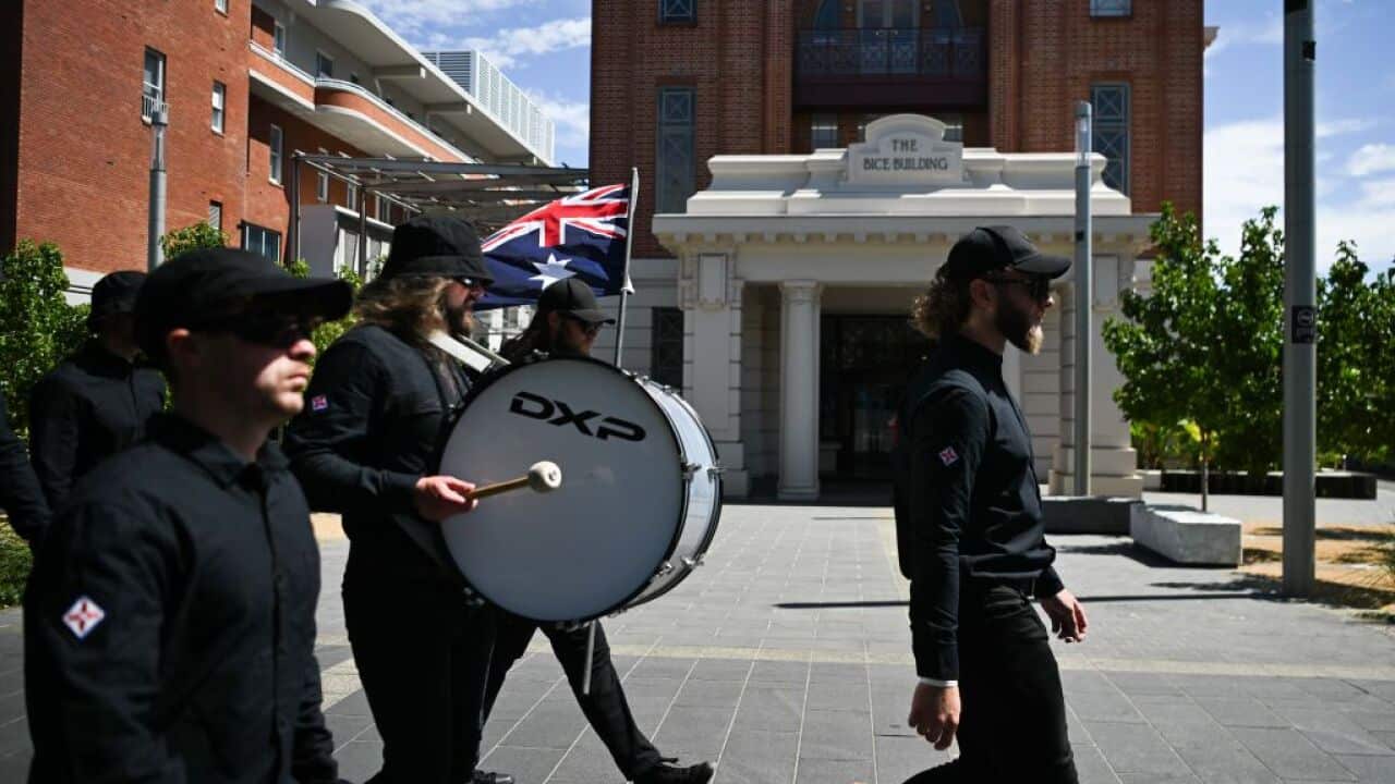 Men dressed in all black marching with a drum and Australian flag