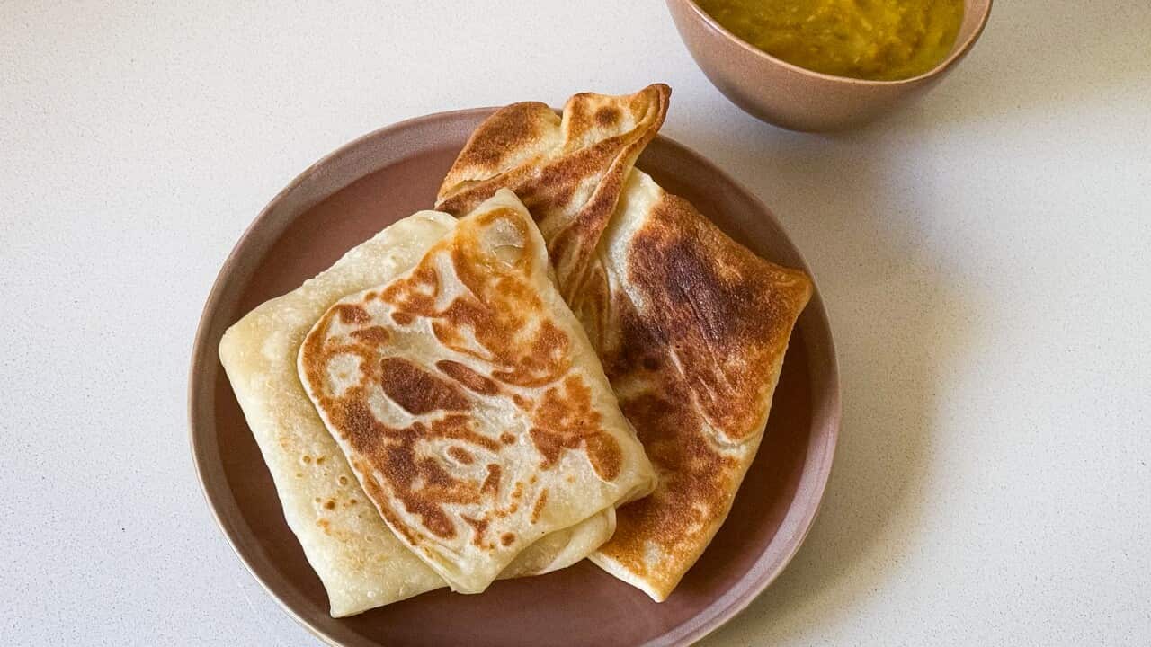Pieces of roti prata sitting on a brown plate, with a bowl of dhal on the side.