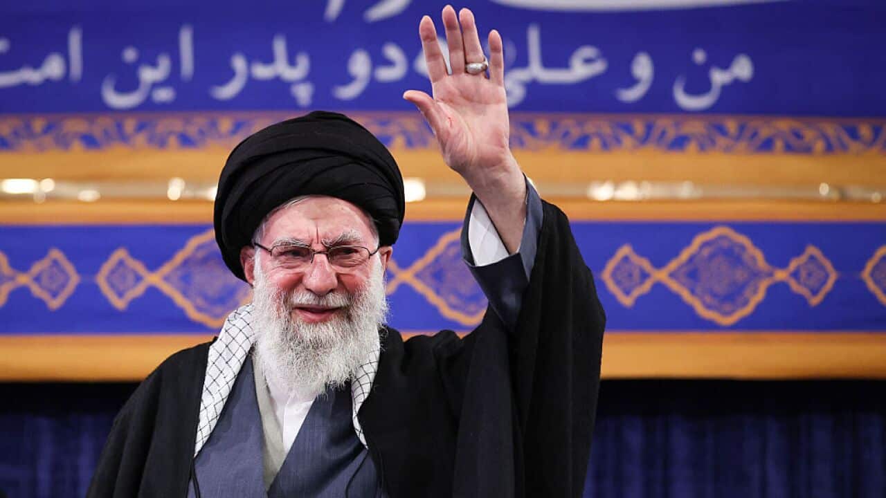 A man in black robes raises his hand smiling