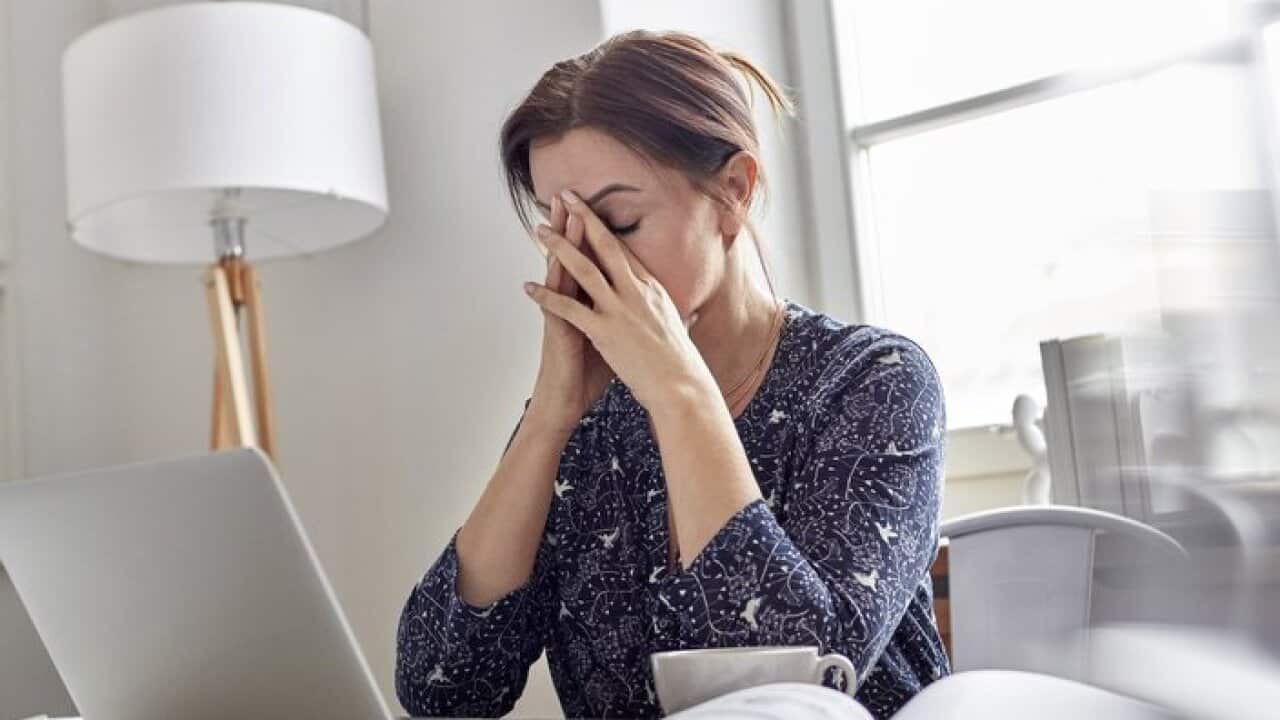 Tired, stressed businesswoman at laptop with head in hands