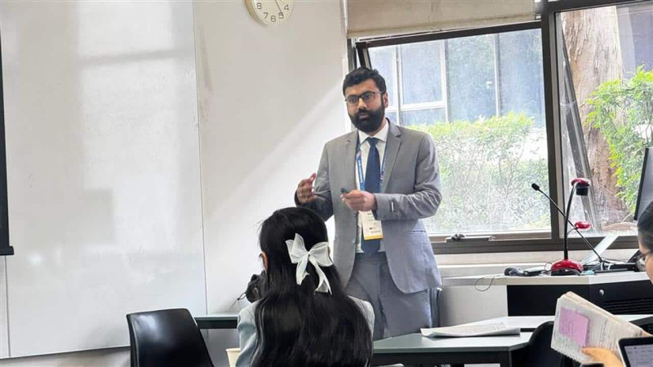 a man from Pakistan wearing suit while giving lecture in a class room