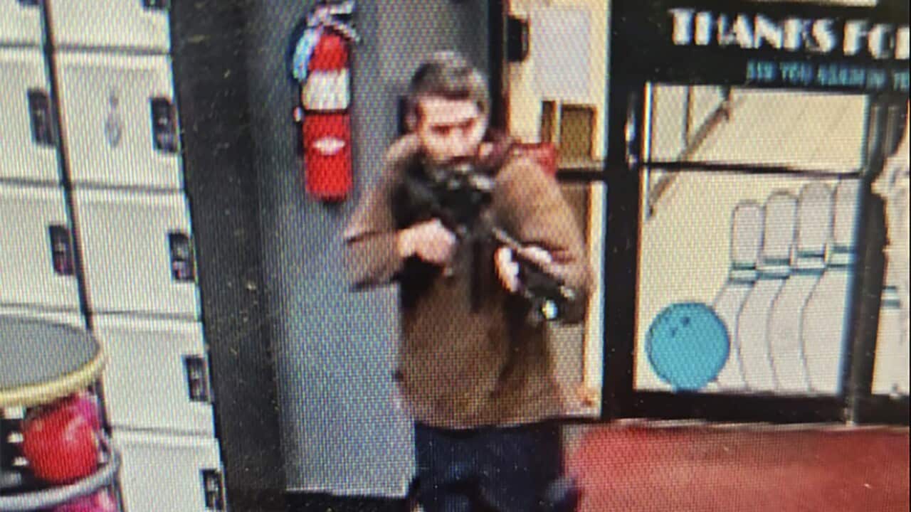 A man holding a rifle in front of the doors of a bowling alley.