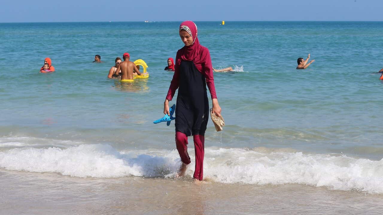 A woman at a beach wearing a maroon burkini.