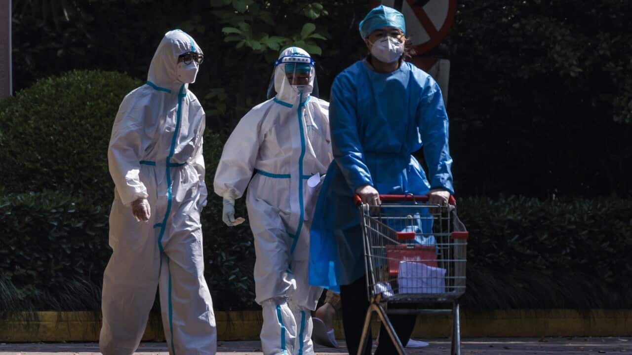 Three people wearing protective gear are seen walking down a street.
