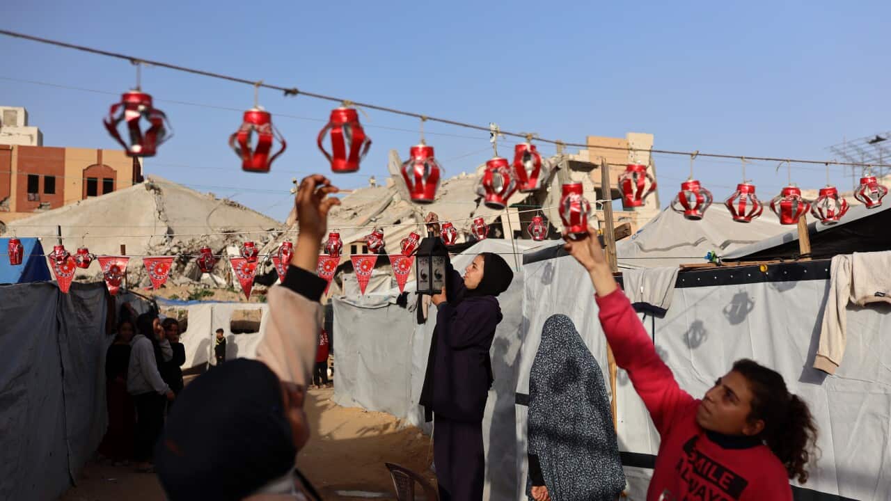 People hanging red lanterns and decorations between tent shelters.