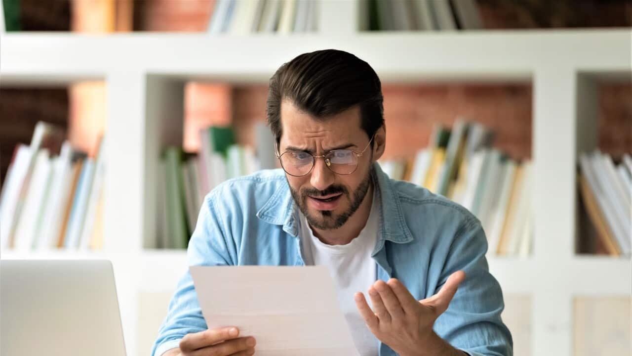 Young man holding paper letter reading shocking unpleasant unexpected news