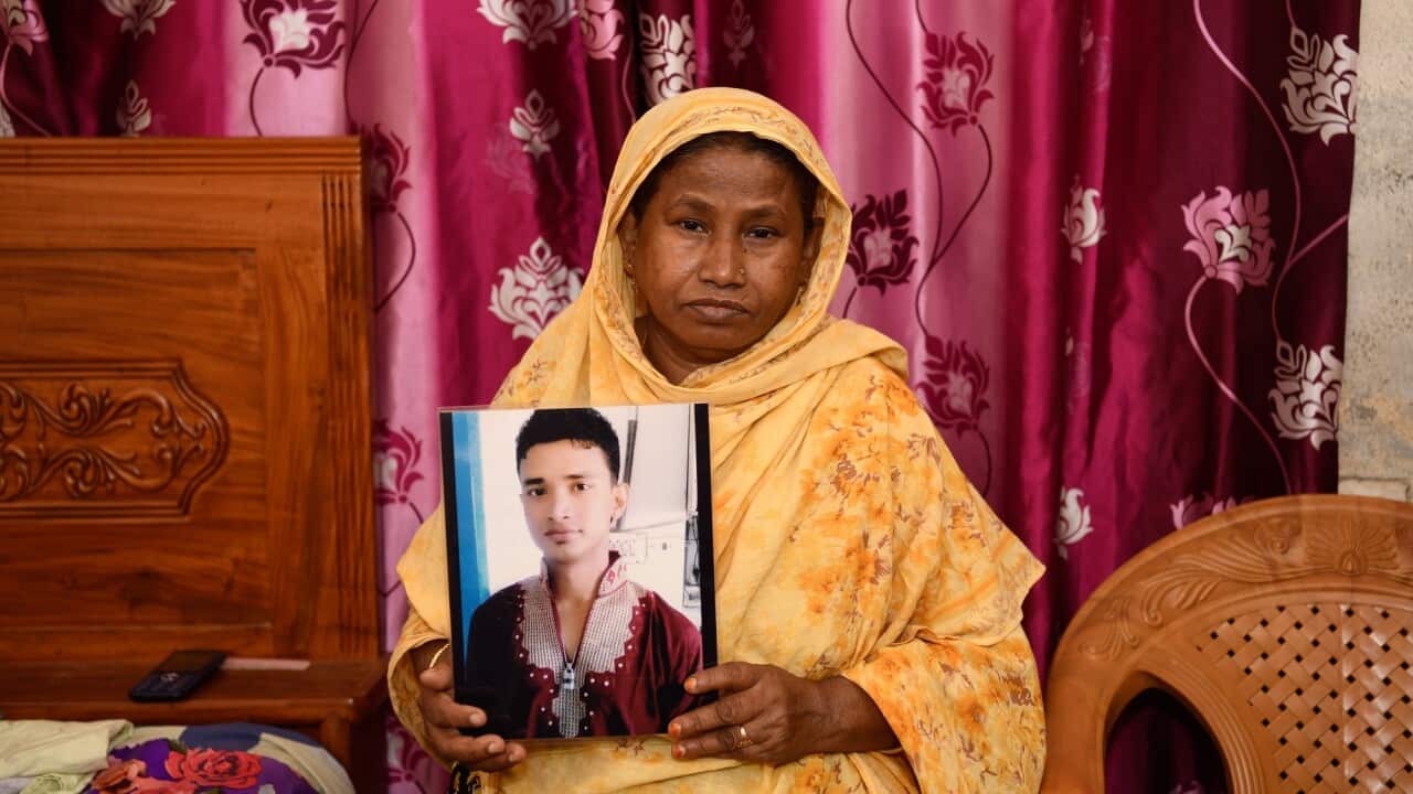 A woman in a yellow sari holds up a photo of her son who died in the Rana Plaza disaster.