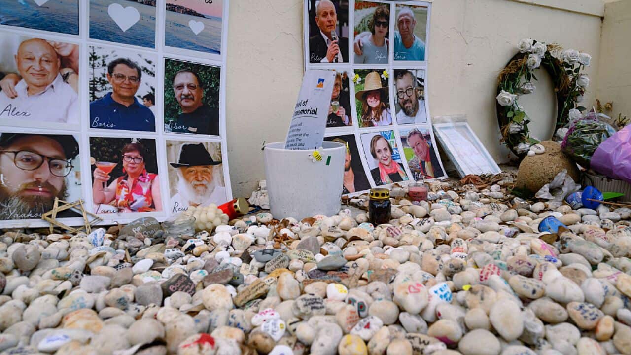 Stones of remembrance and photos are seen outside by a wall.