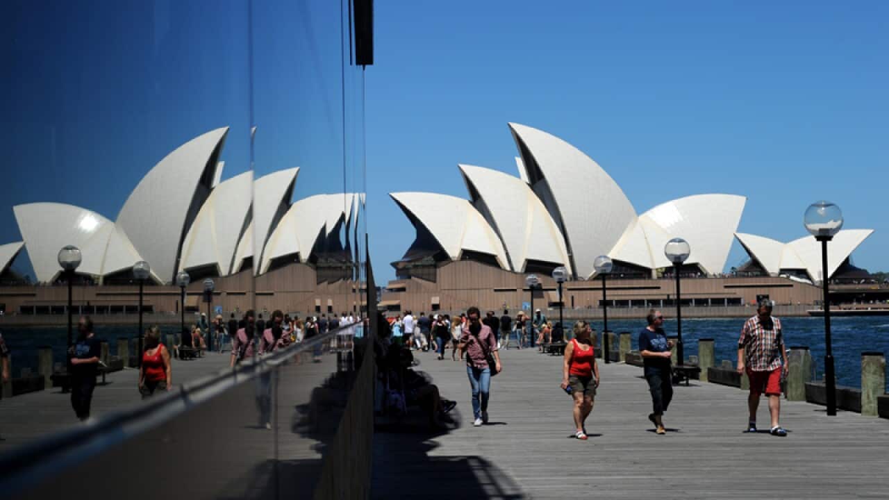Tourists walk toward the Sydney Opera House.