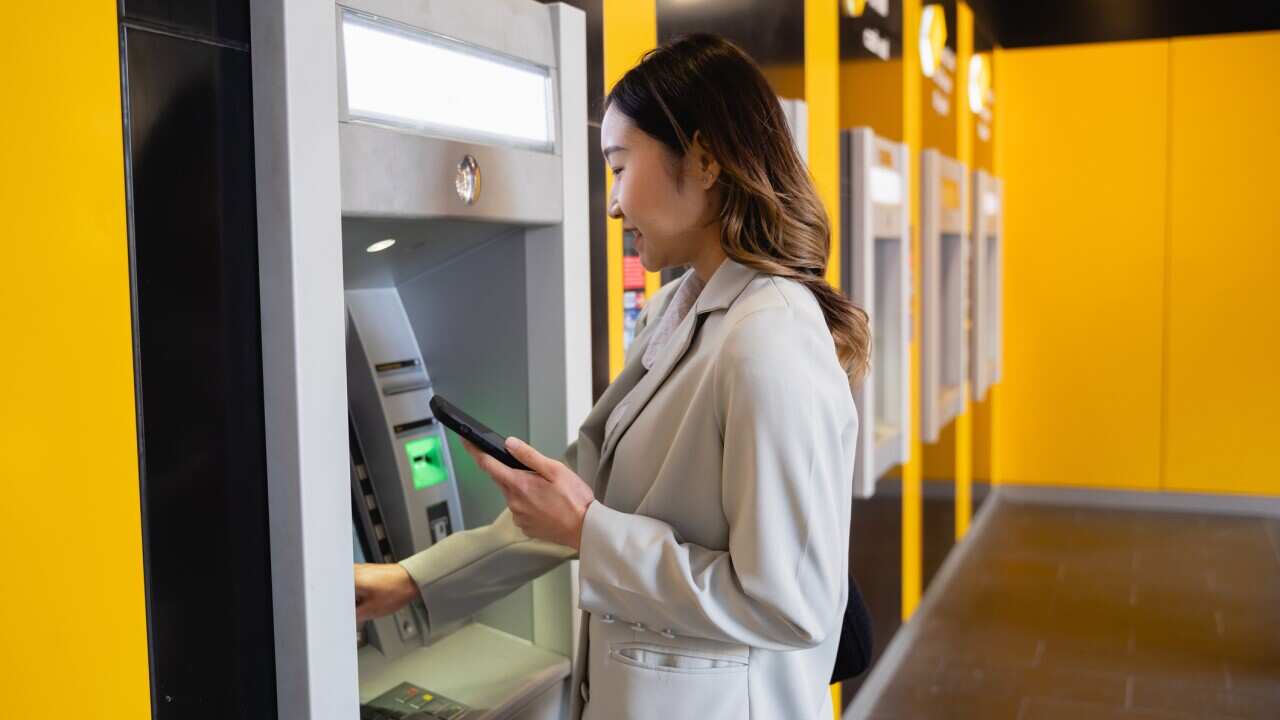 Young Asian woman using mobile phone while paying for online shopping at ATM machine