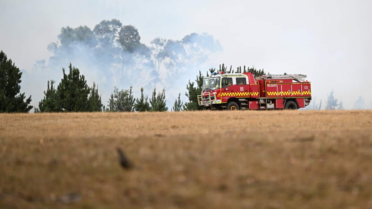 A red fire truck drives past dry grass