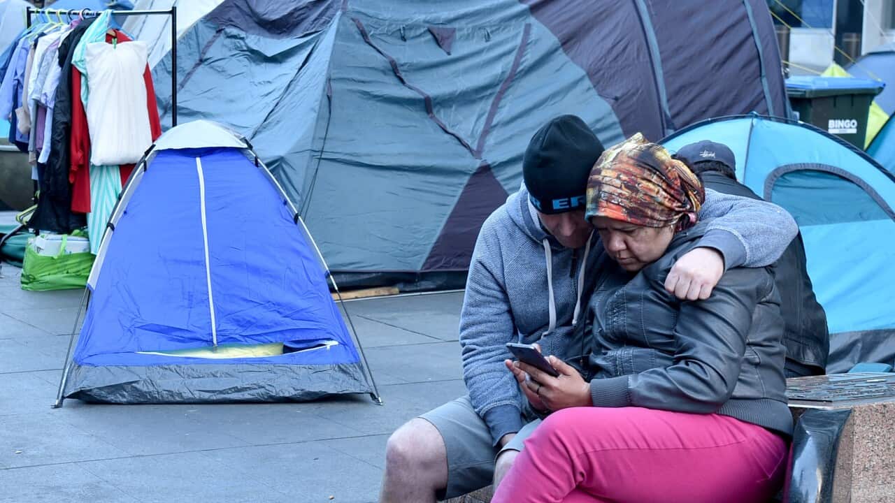 A homeless couple (R) look at a mobile phone in front of tents set up