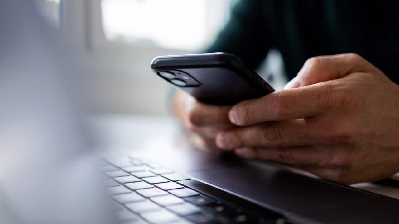 A hand holding a phone above a laptop keyboard.