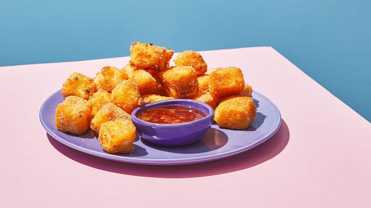 Golden crumbed cubes sit on a pale purple plate, along with a bowl of red sauce.