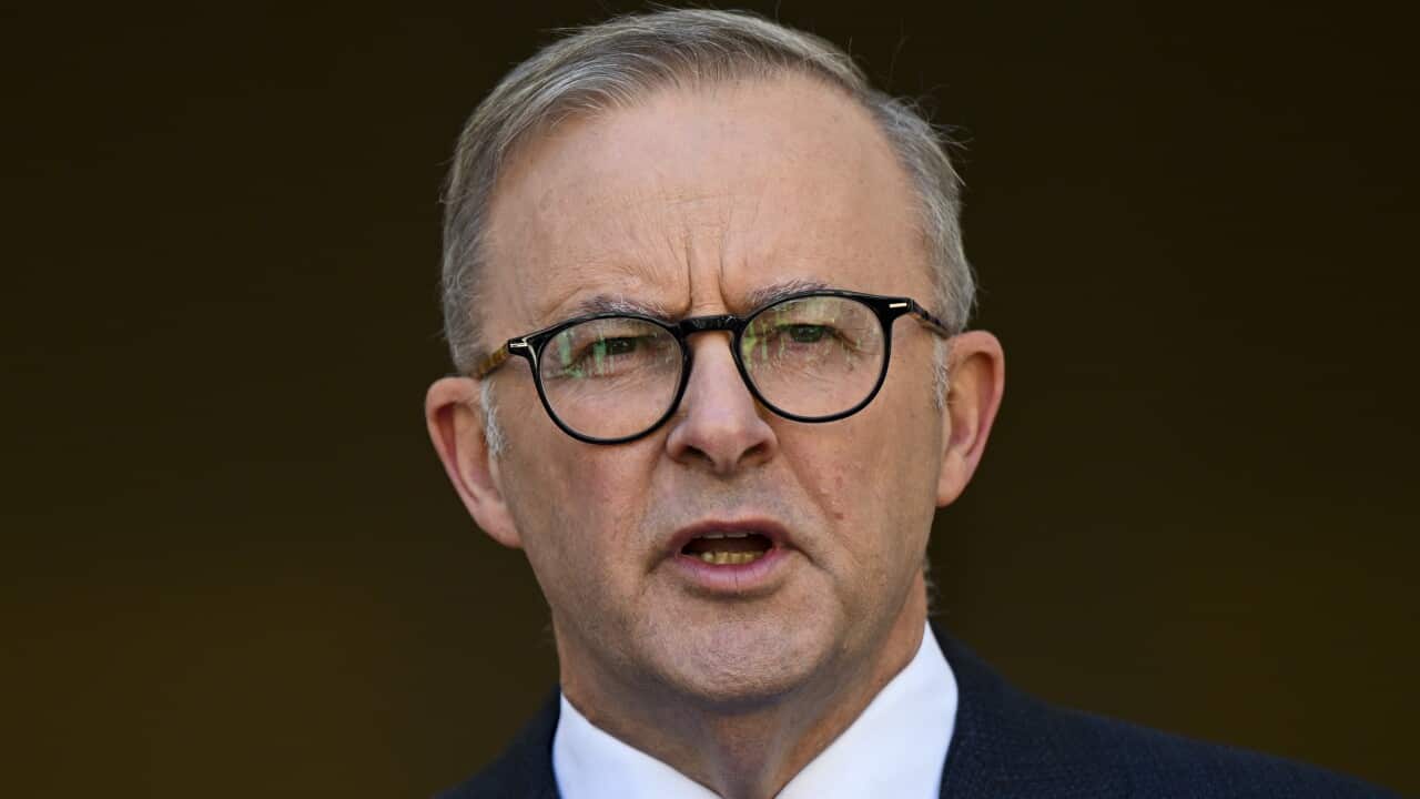 Man in suit and glasses mid-speech.