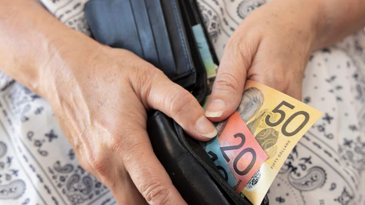 An adult holding a wallet containing some Australian bank notes.