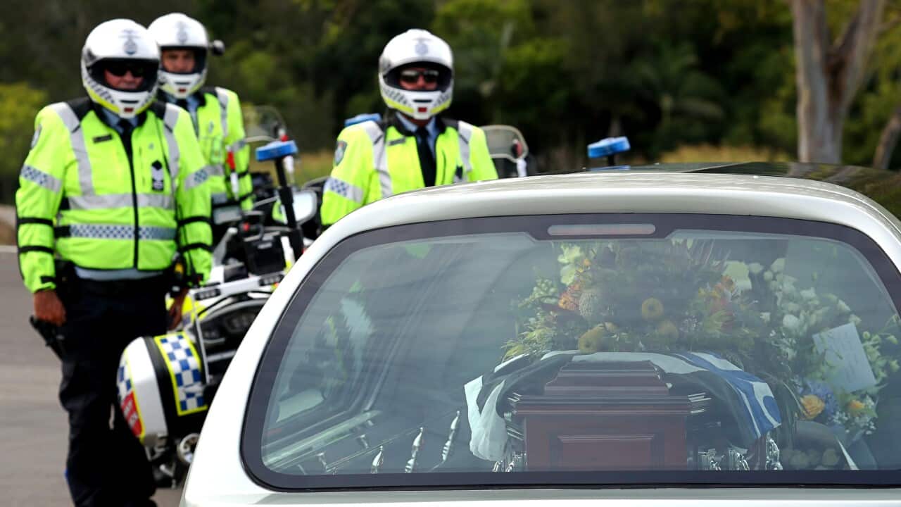 Uniformed and helmet-wearing motorcycle police look on at a silver hearse with a coffin inside.
