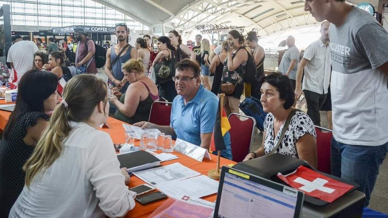 Stranded tourists listen to officers at Denpasar airport in Bali.